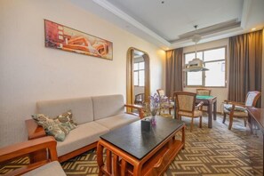 Habitación de hotel con sofá, una mesa de centro, una mesa de comedor con sillas, un espejo grande y un cuadro en la pared.
