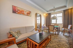 Quarto de hotel com sofá, mesa de centro, mesa de jantar com cadeiras, um espelho grande e um quadro na parede.