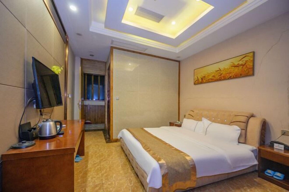 Habitación de hotel con cama, escritorio con hervidor, televisor y un cuadro en la pared.