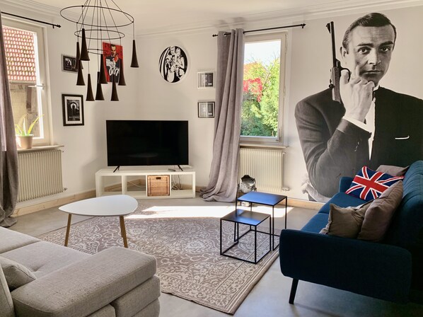 A living room with a flat-screen TV, a small table, a sofa, and a decorative wall.