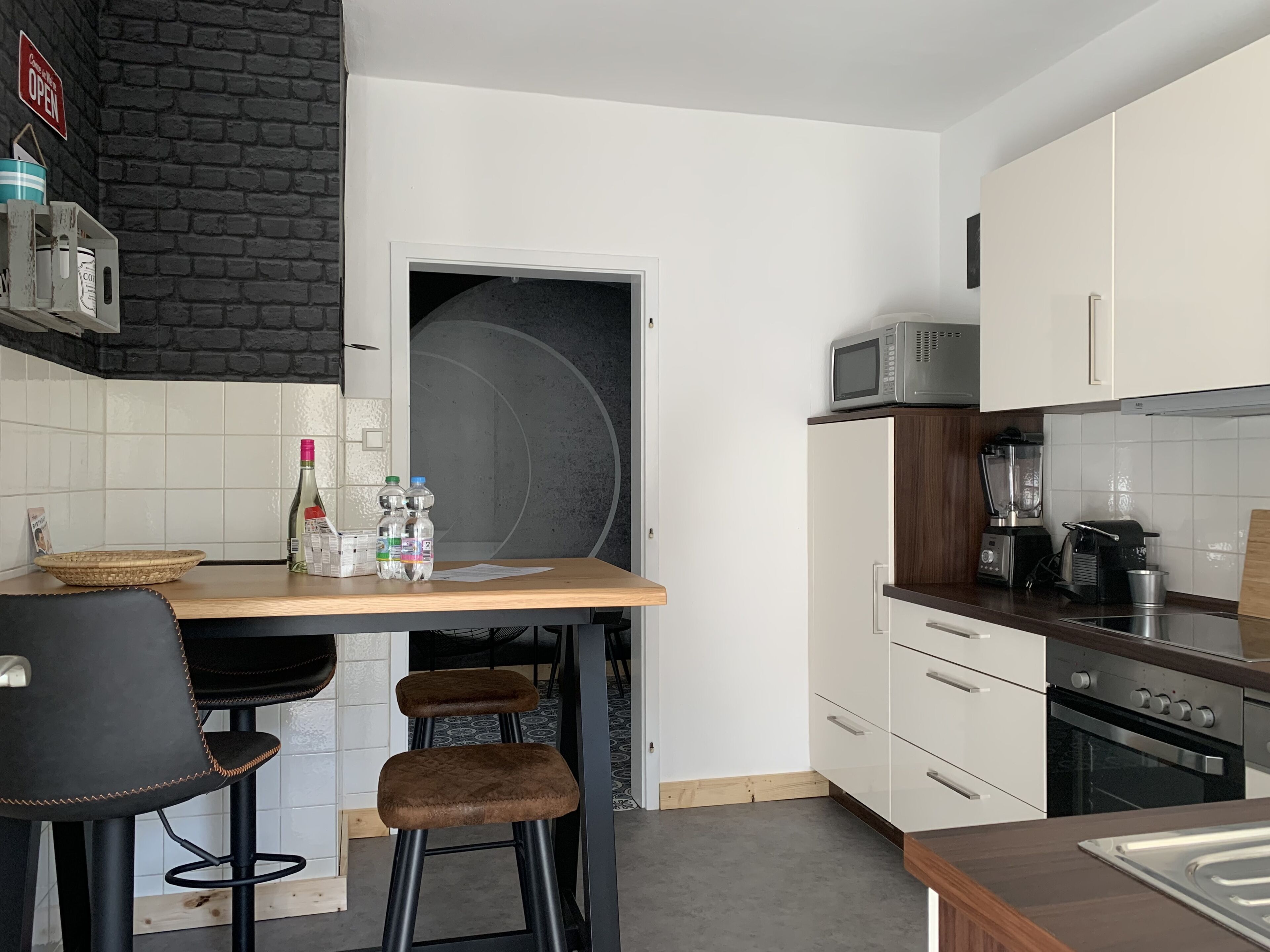 Une cuisine compacte avec un plan de travail en bois, un four à micro-ondes, un mixeur et une cuisinière. Il y a deux tabourets et une chaise.