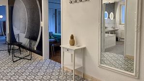 A modern hotel room with a large mirror, a chandelier, a small table with a pineapple, and a view into the bathroom.
