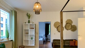 A living room with a wooden herringbone floor, a green sofa, a white shelving unit, and a hanging light fixture.