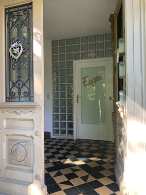 A hallway with a checkered floor, a decorative metal gate, a frosted glass door with the name 'Eugen' on it, and a tiled wall.