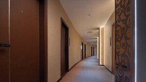 Un pasillo largo y estrecho en un hotel, con puertas a ambos lados y un zócalo decorativo a la derecha.