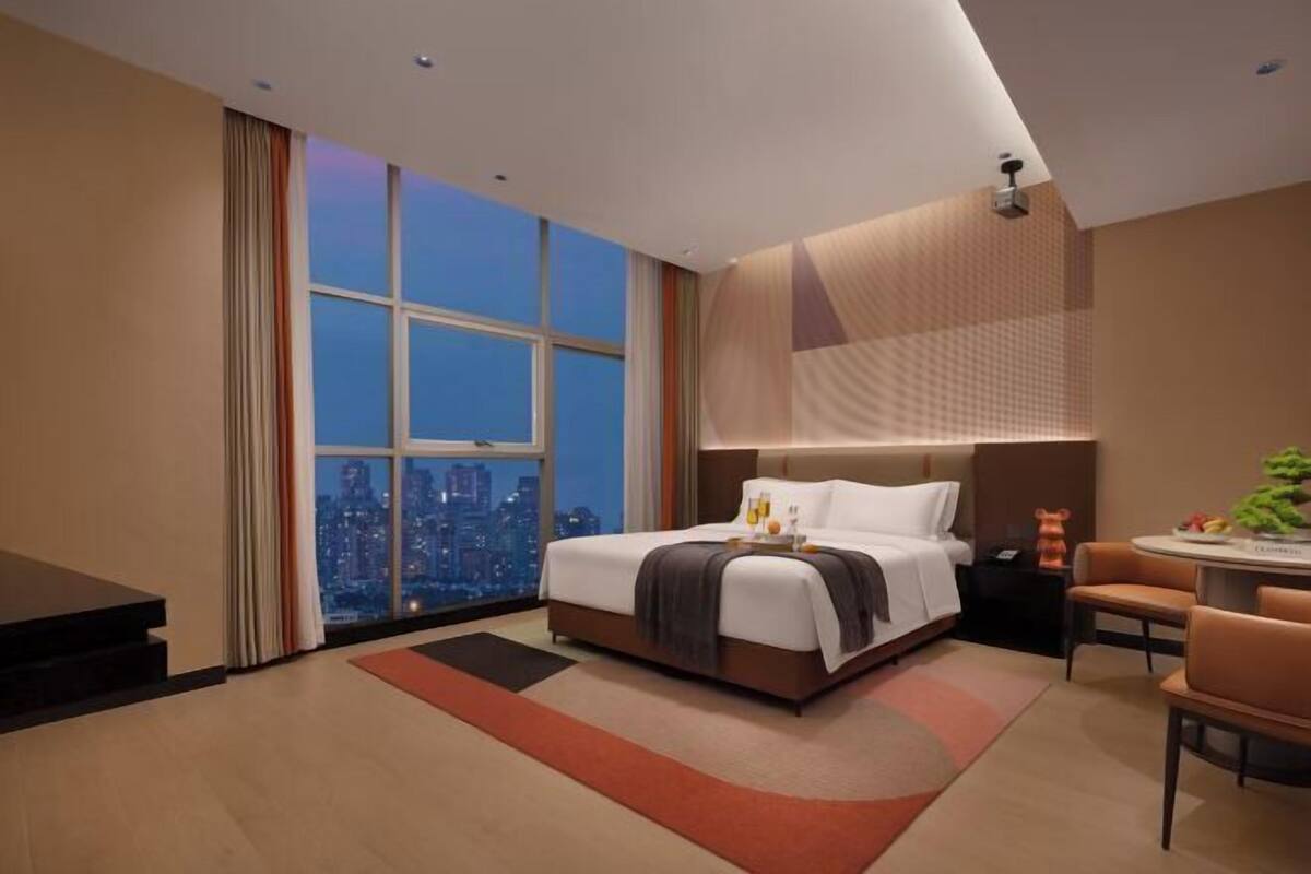 A modern hotel room with a large window, a bed, a desk, and a chair.