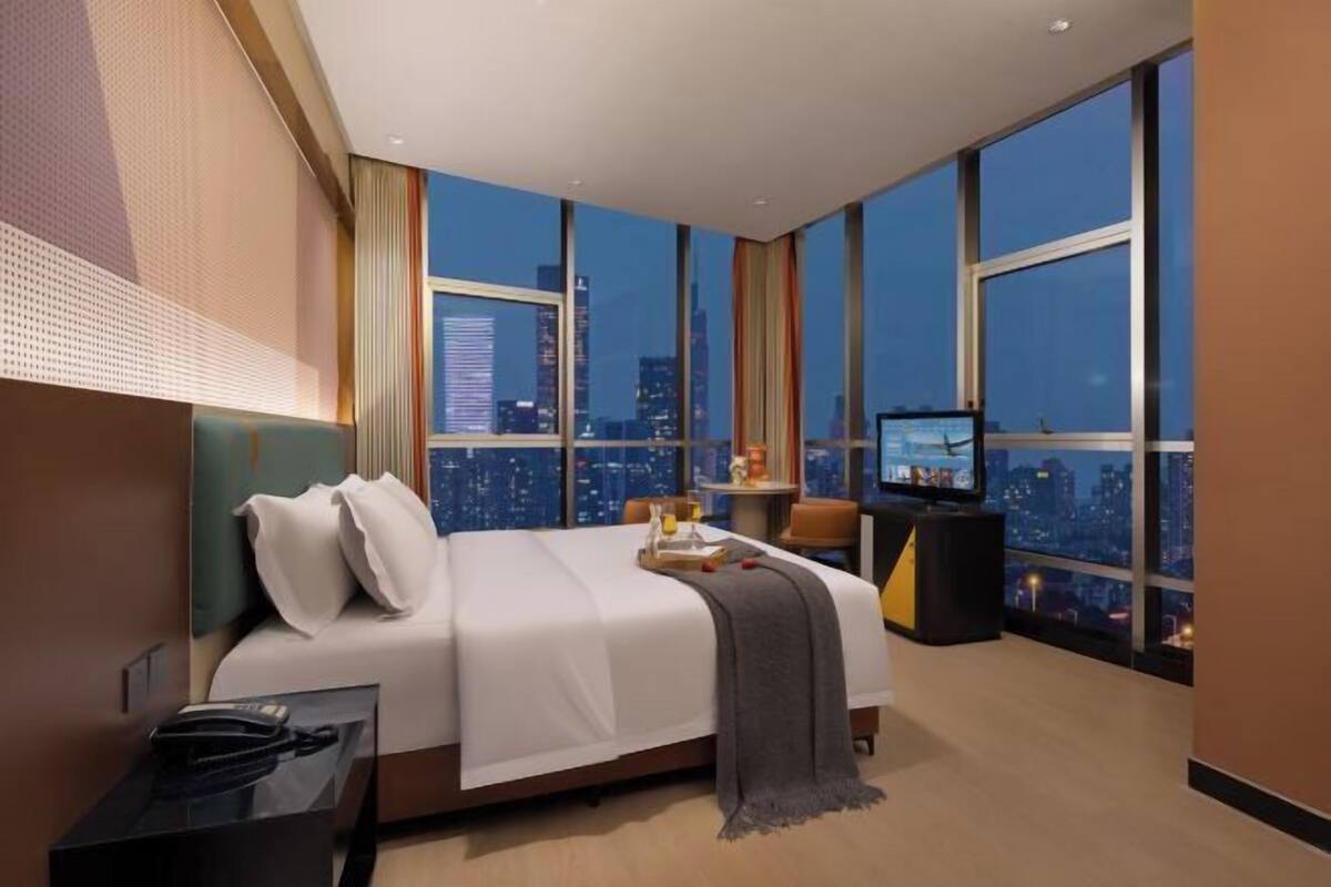 A modern hotel room with a large bed, a television, a desk, and a city view.