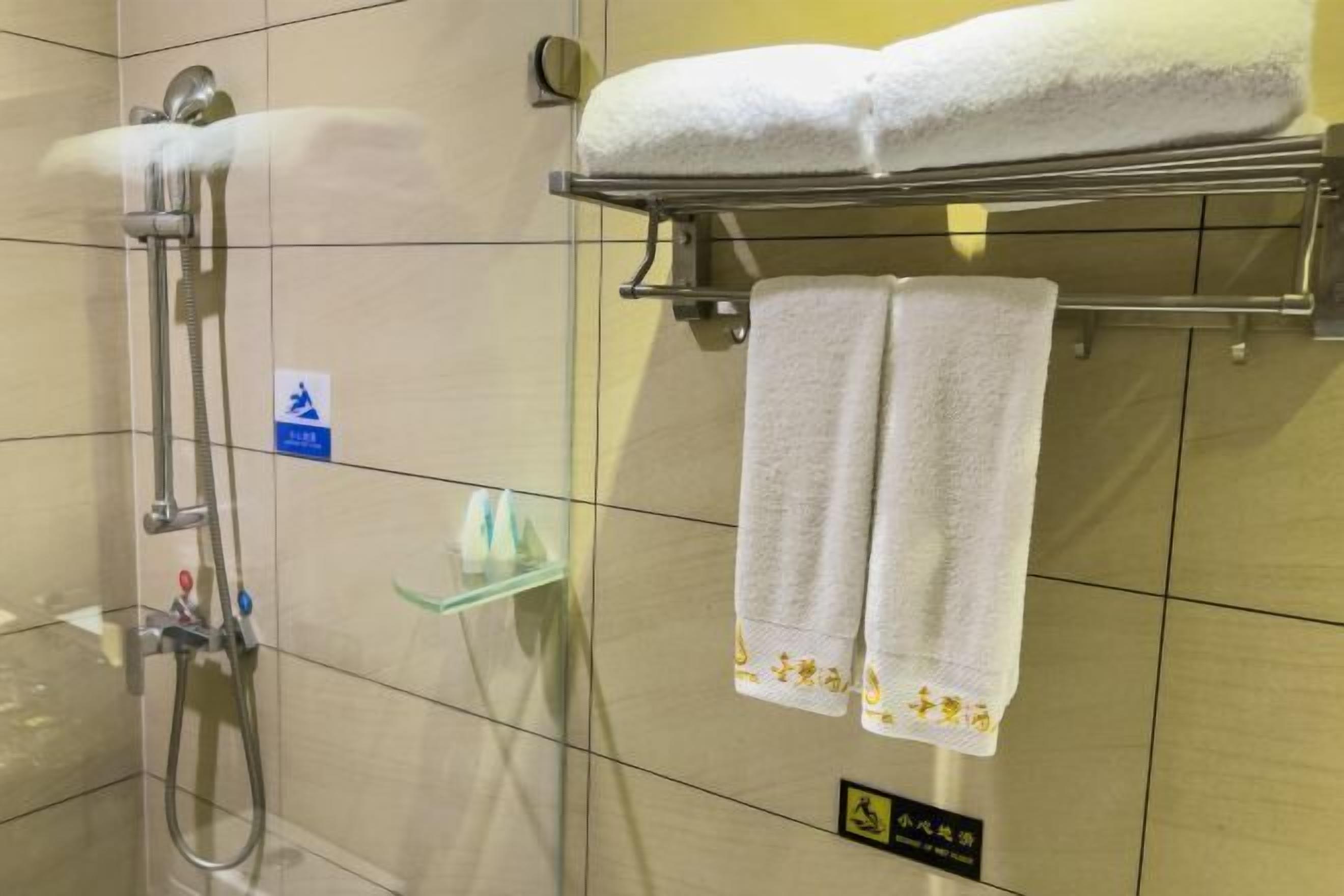 A bathroom with a shower, two towels on a rack, and a glass shelf.