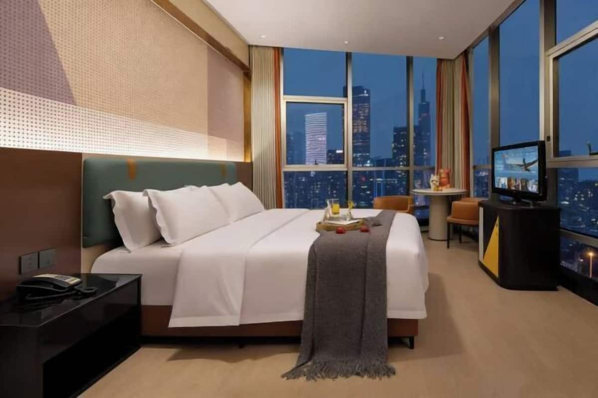 A hotel room with a bed, a desk, a TV, and a city view.
