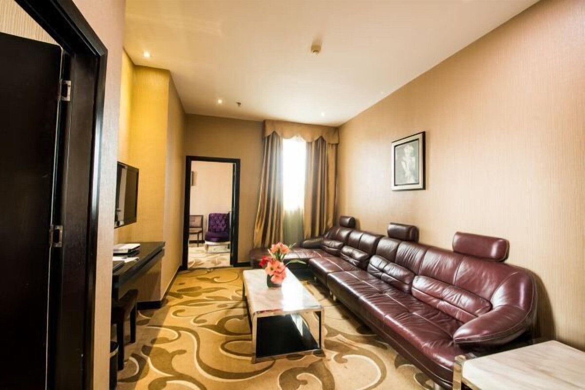 A hotel room with a large leather sofa, a small table with a vase, a desk, and a chair.