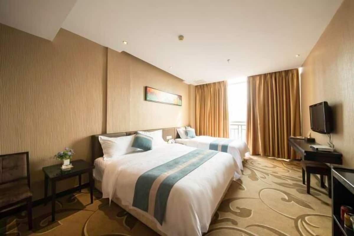 A hotel room with two beds, a TV, a desk, and a window with curtains.