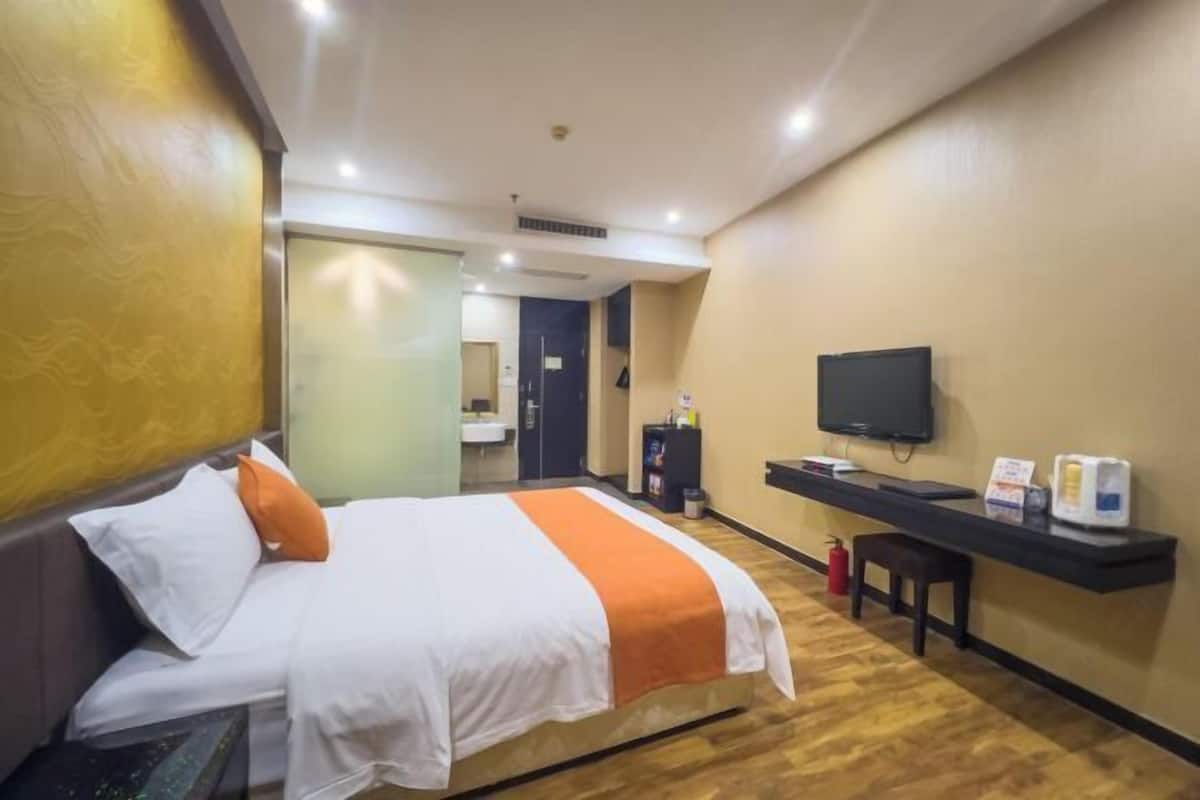 A hotel room with a bed, a television, a desk with a computer, and a fire extinguisher.