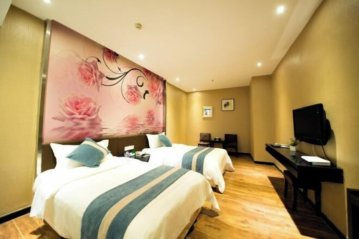 A hotel room with two beds, a desk, a TV, and a large floral mural on the wall.
