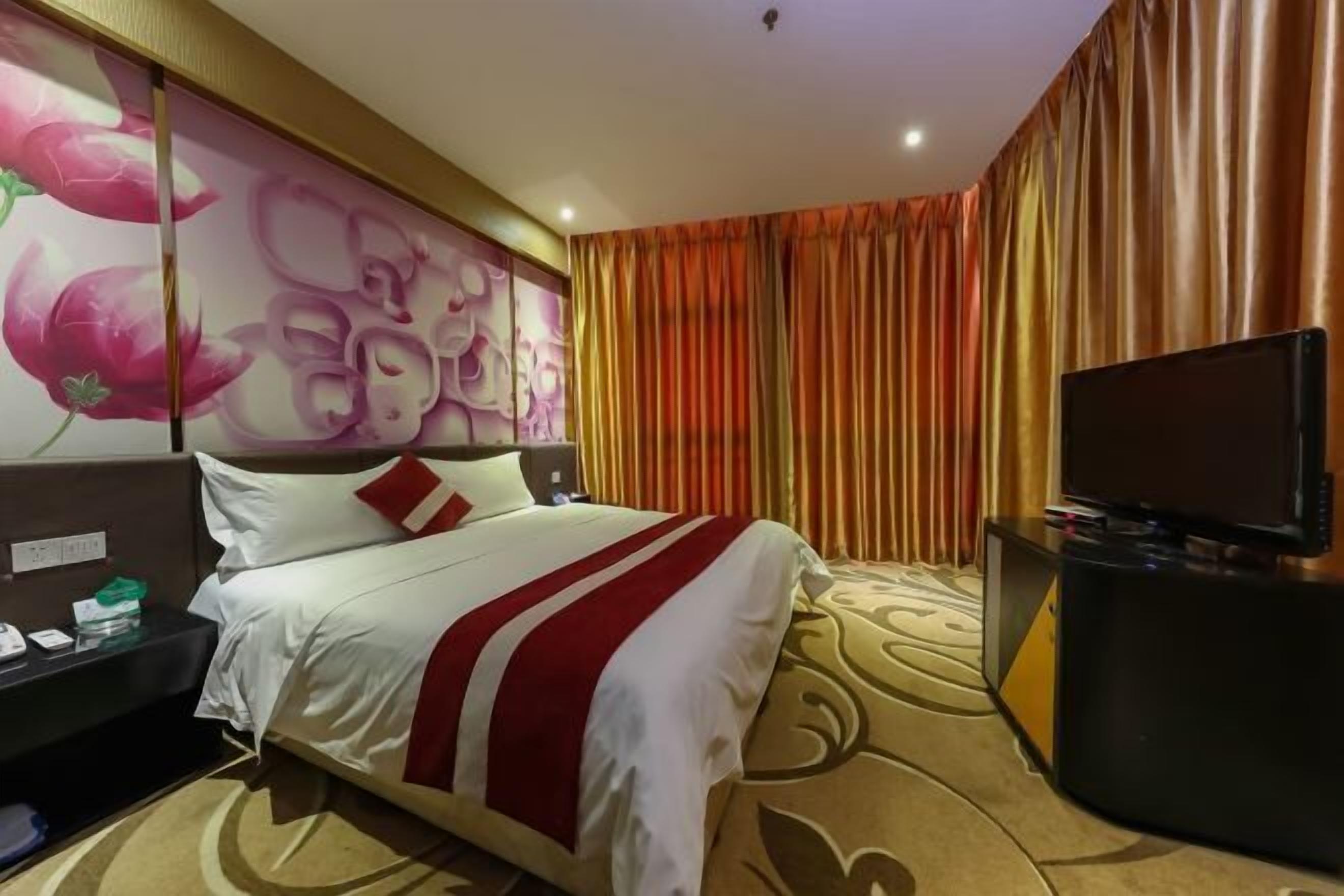 A hotel room with a bed, a TV, and a wall with floral artwork.