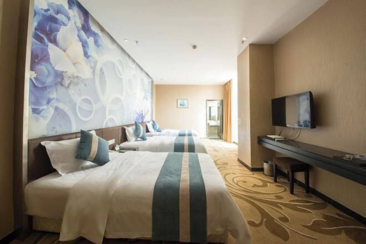 A hotel room with two beds, a TV, a desk, and a large floral mural on the wall.