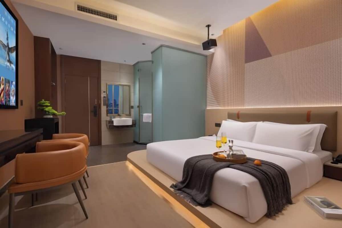 A modern hotel room with a large bed, a desk with chairs, a bathroom, and a TV.