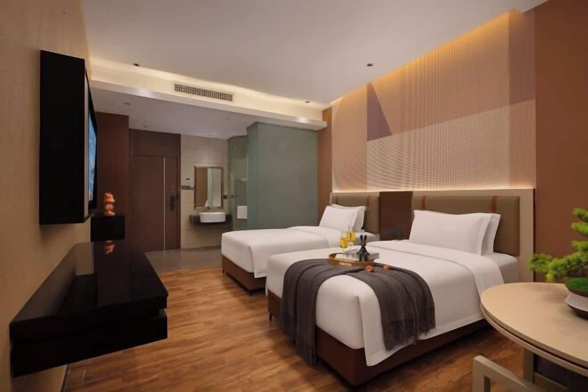 A hotel room with two beds, a TV, a desk, and a small table with a plant.
