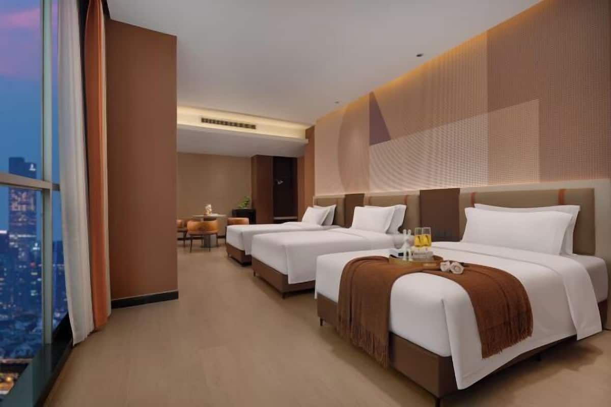 A hotel room with two beds, a desk, and a view of the cityscape.