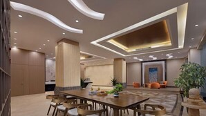 Un moderno vestíbulo de hotel con una larga mesa de madera y sillas, un gran pilar y una zona de estar con sillas color naranja.