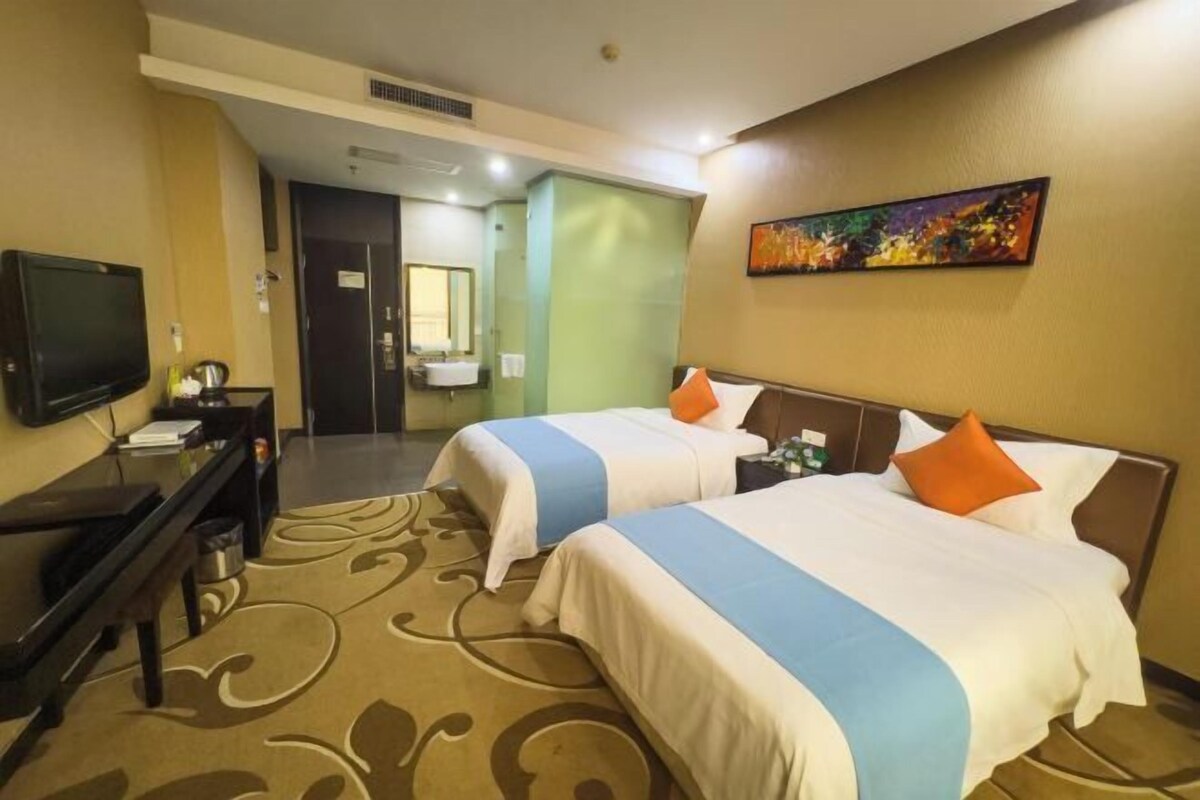 A hotel room with two beds, a television, a desk, and a bathroom visible through an open door.