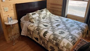 Een slaapkamer in chaletstijl met een bed, nachtkastje en raam met uitzicht op een besneeerd landschap.
