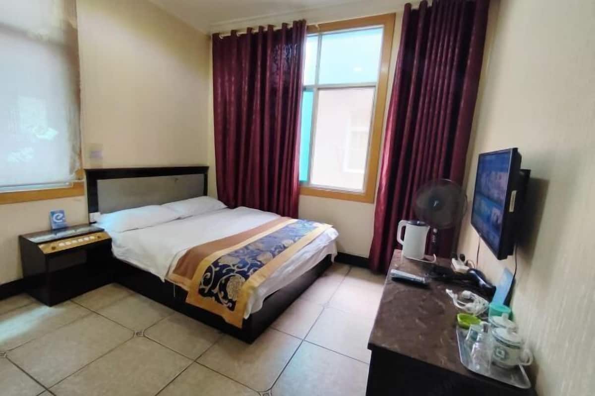 Ein Hotelzimmer mit Bett, Nachttisch, Schreibtisch mit Computer, Fenster mit Vorhängen und Fernseher.