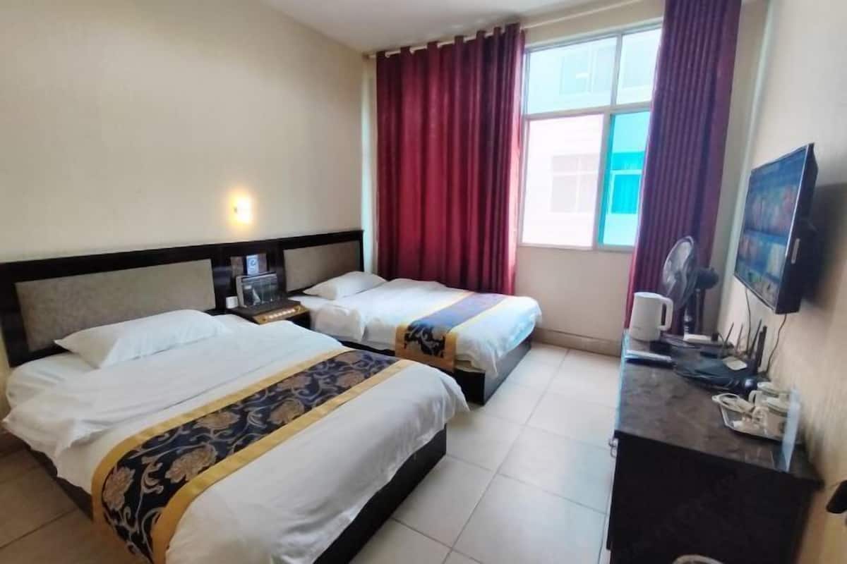 Ein Hotelzimmer mit zwei Betten, einem Schreibtisch mit Computer, einem Fernseher und einem Fenster mit Vorhängen.