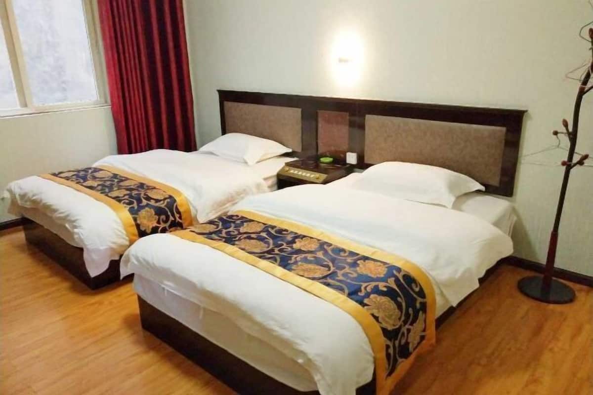 Ein Hotelzimmer mit zwei Betten, einem Nachttisch, einer Lampe und einem Fenster mit Vorhängen.