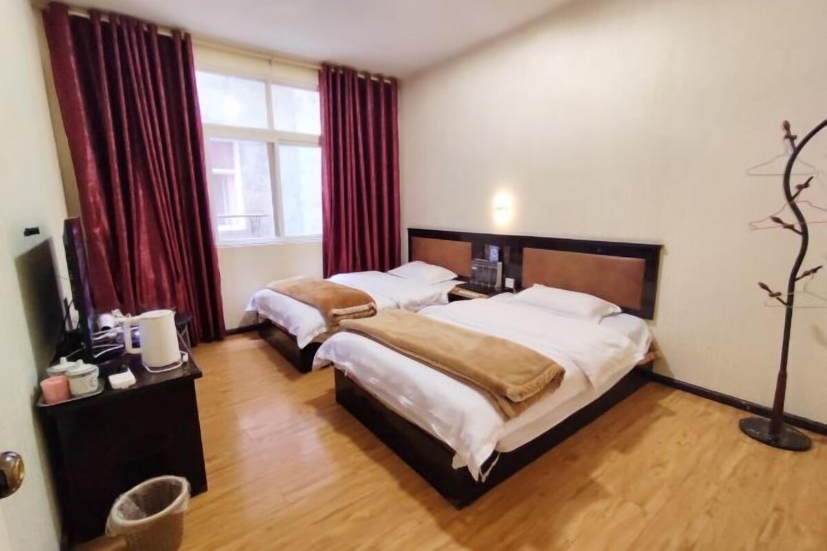 Quarto de hotel com duas camas, uma mesa com cadeira, televisão e janela com cortinas.