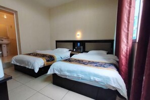 Quarto de hotel com duas camas, uma mesa de cabeceira, luminária na parede e janela com cortinas.