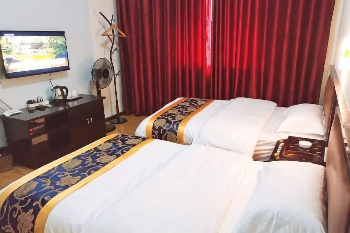 Ein Hotelzimmer mit zwei Betten, einem Fernseher, einem Schreibtisch und einem roten Vorhang.