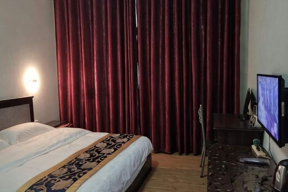 Ein Hotelzimmer mit Bett, Schreibtisch mit Computer, Fernseher und einem roten Vorhang.