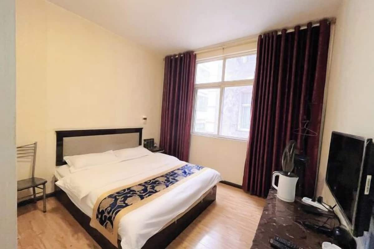 Ein Hotelzimmer mit einem Bett, einem Fernseher, einem Schreibtisch und einem Fenster mit Vorhängen.