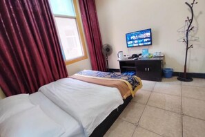 Quarto de hotel com cama, escrivaninha com computador, televisão e janela com cortinas.