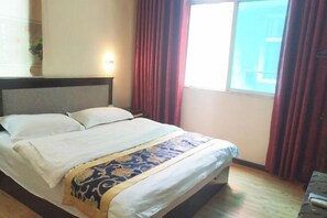 Quarto de hotel com cama, mesa de cabeceira, janela com cortinas e luminária na parede.