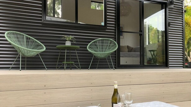 A wooden deck with two cushioned seating areas, a bottle of wine, and two glasses.