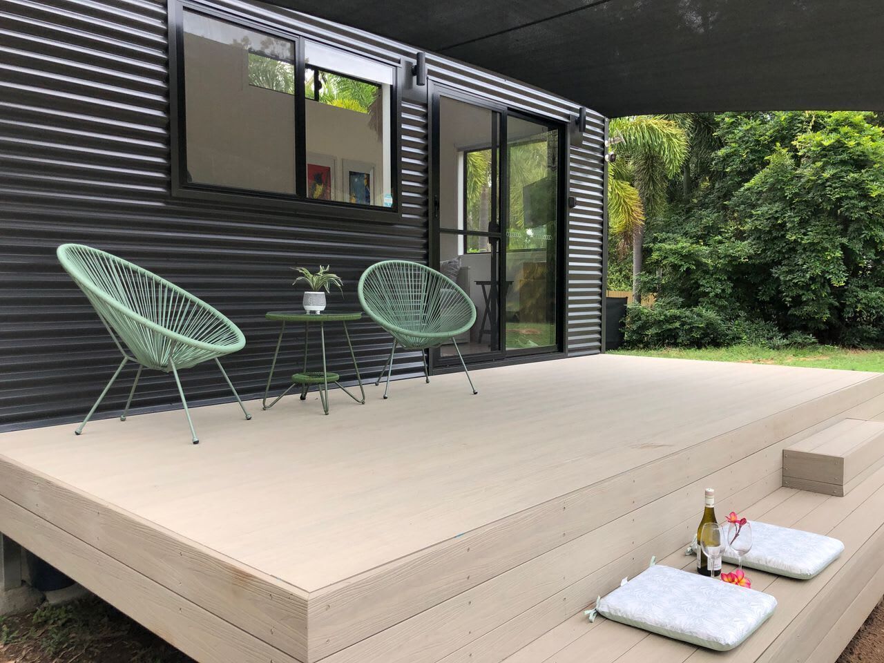 A modern outdoor patio with two green chairs, a small table, and a wine bottle.