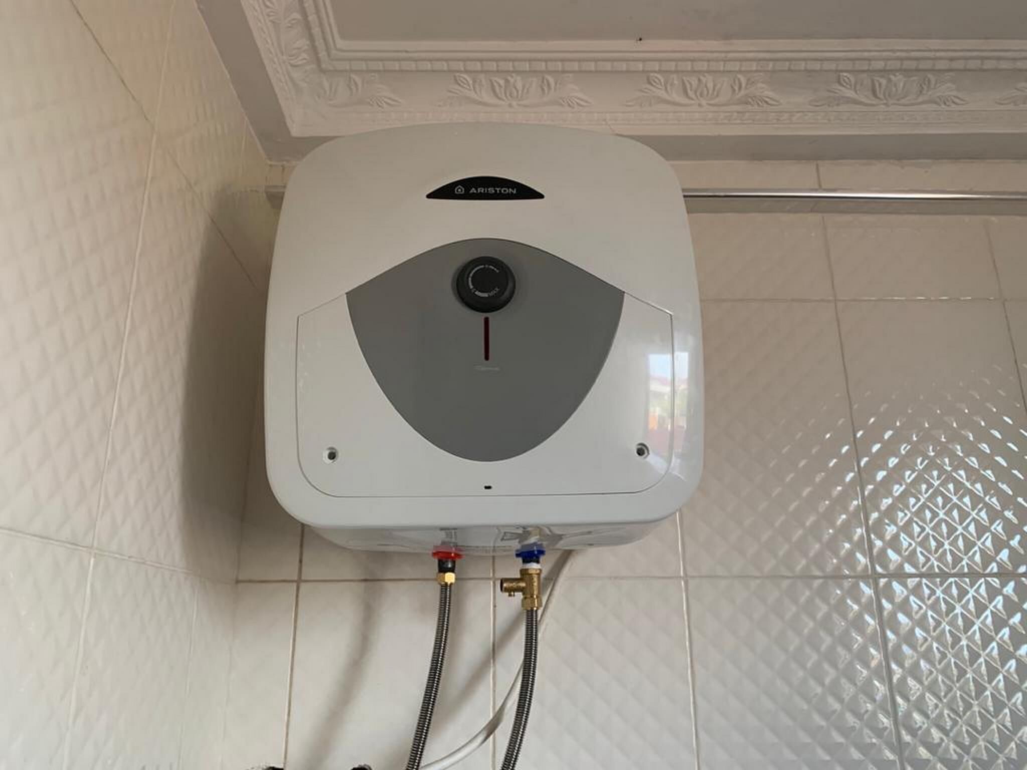 Un chauffe-eau blanc fixé sur un mur recouvert de carreaux, avec un plafond décoratif.