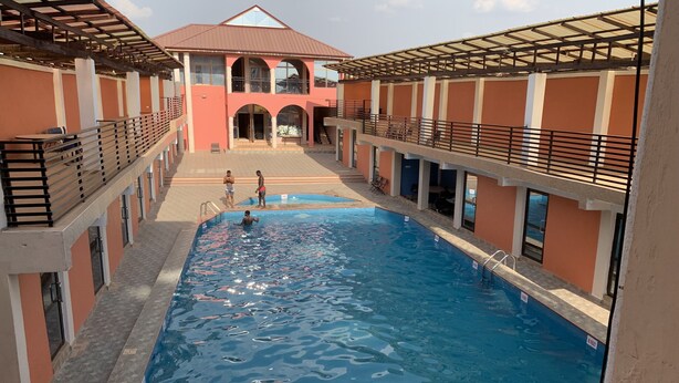 A swimming pool with a view of a building with balconies and a covered walkway. - SWATSON HOTEL (Kumasi)