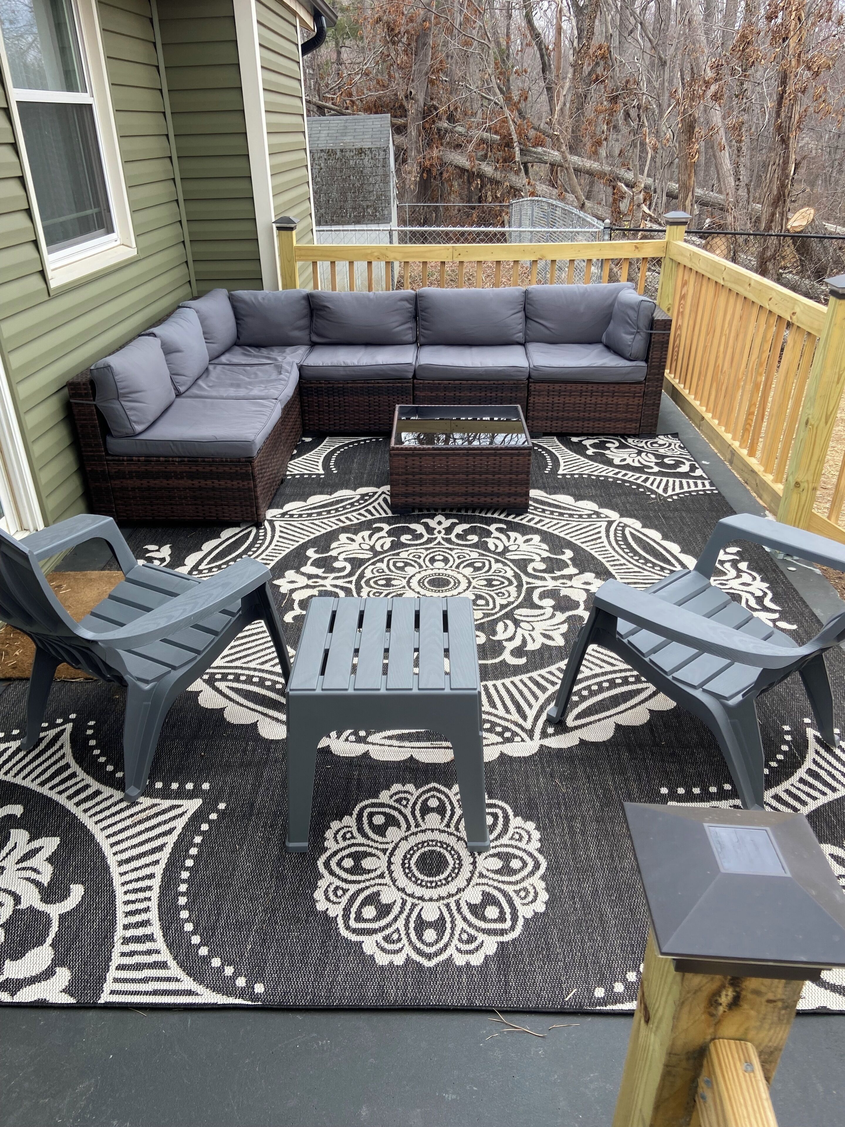 A covered outdoor seating area with a sectional sofa, two chairs, a coffee table, and a decorative rug.