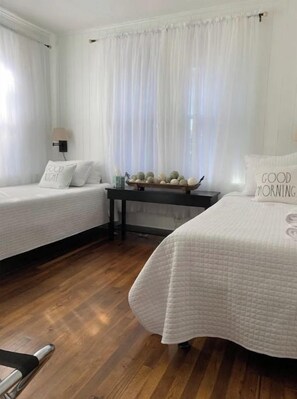 A bedroom with two beds, a nightstand, and a window with sheer curtains.