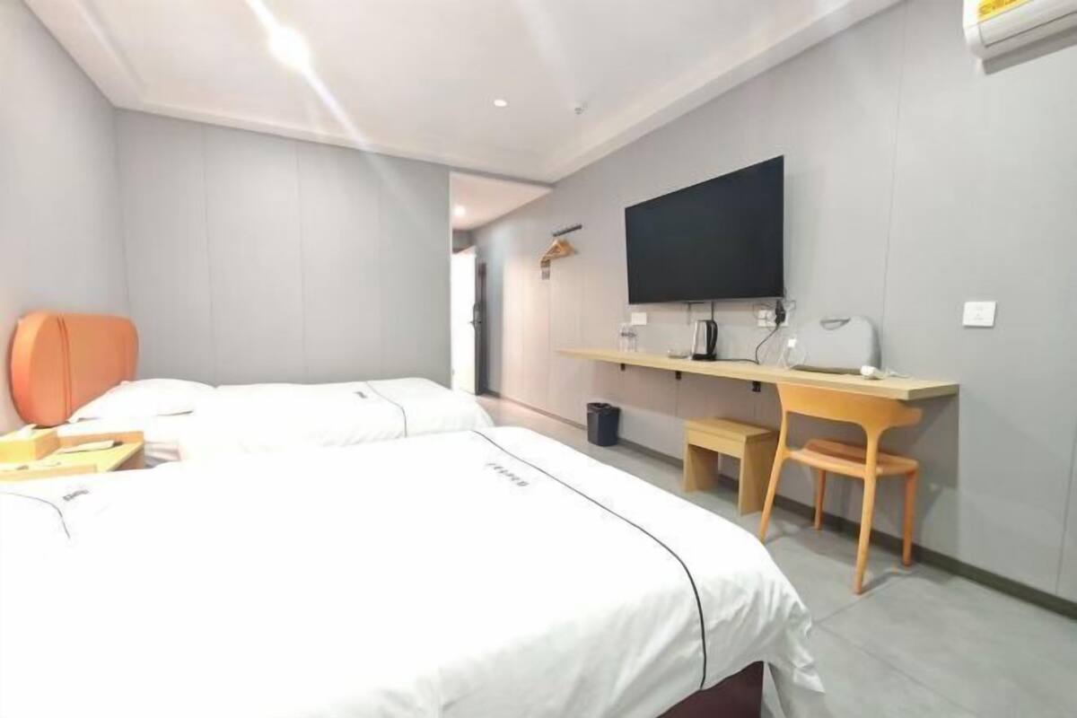 A hotel room with a bed, a desk, a chair, a TV, and a small shelf.