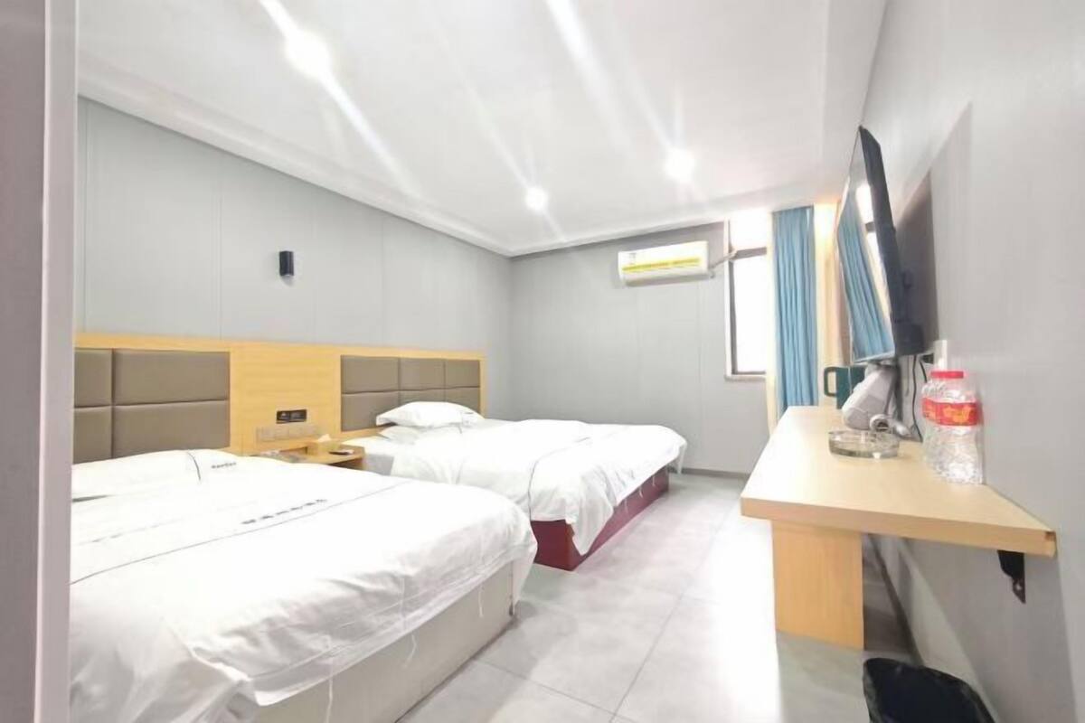 A hotel room with two beds, a desk, a TV, and an air conditioning unit.