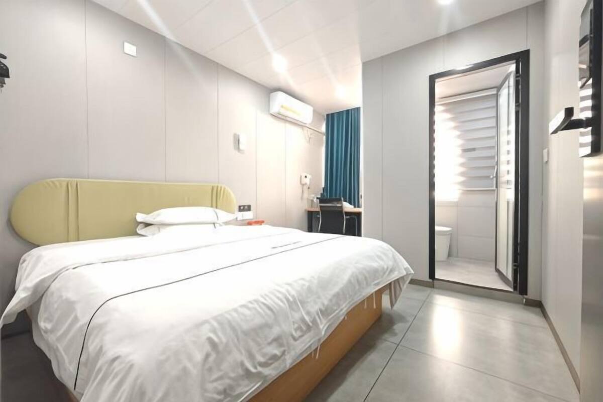 A hotel room with a bed, a desk, a chair, a mirror, and a door leading to a bathroom.