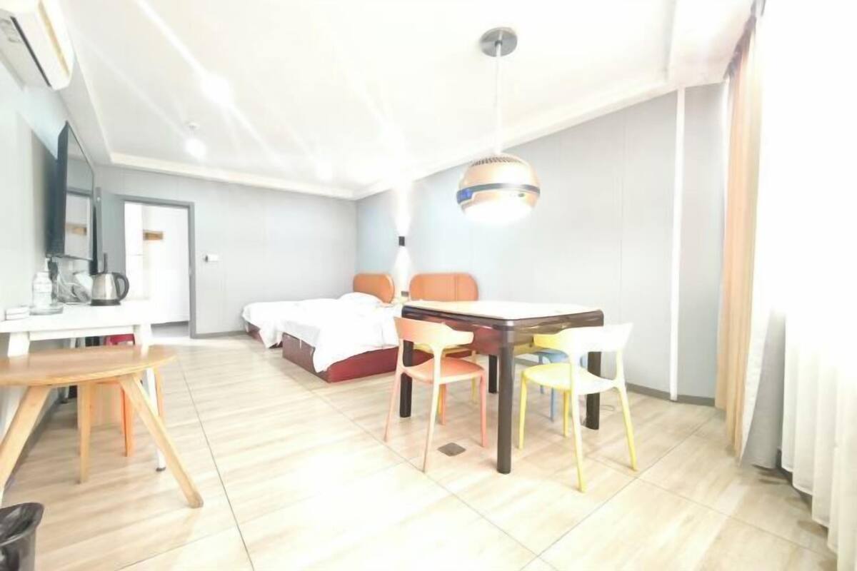 A hotel room with a bed, a desk, a chair, a table, and a hanging light fixture.
