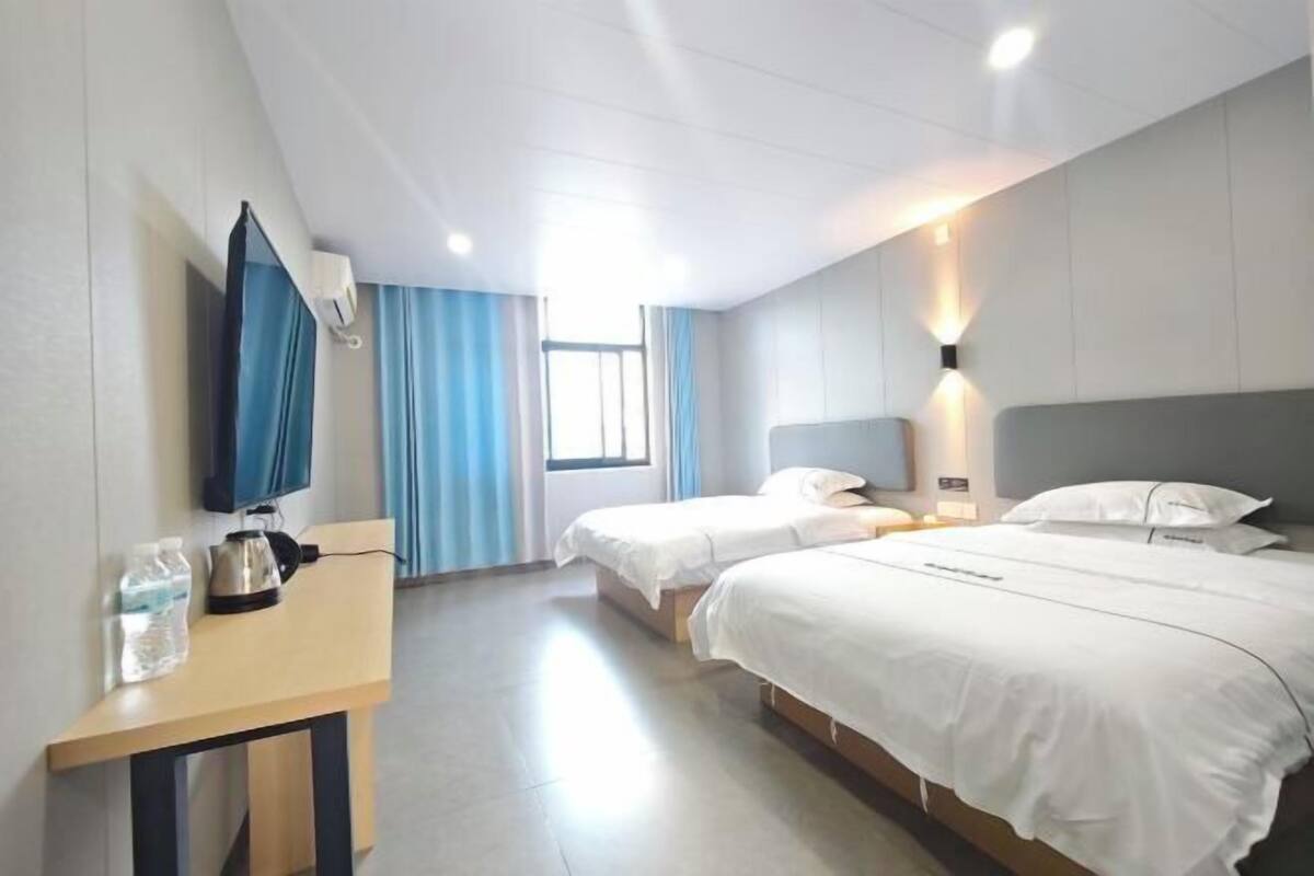 A hotel room with two beds, a desk with a chair, a television, and a window with curtains.