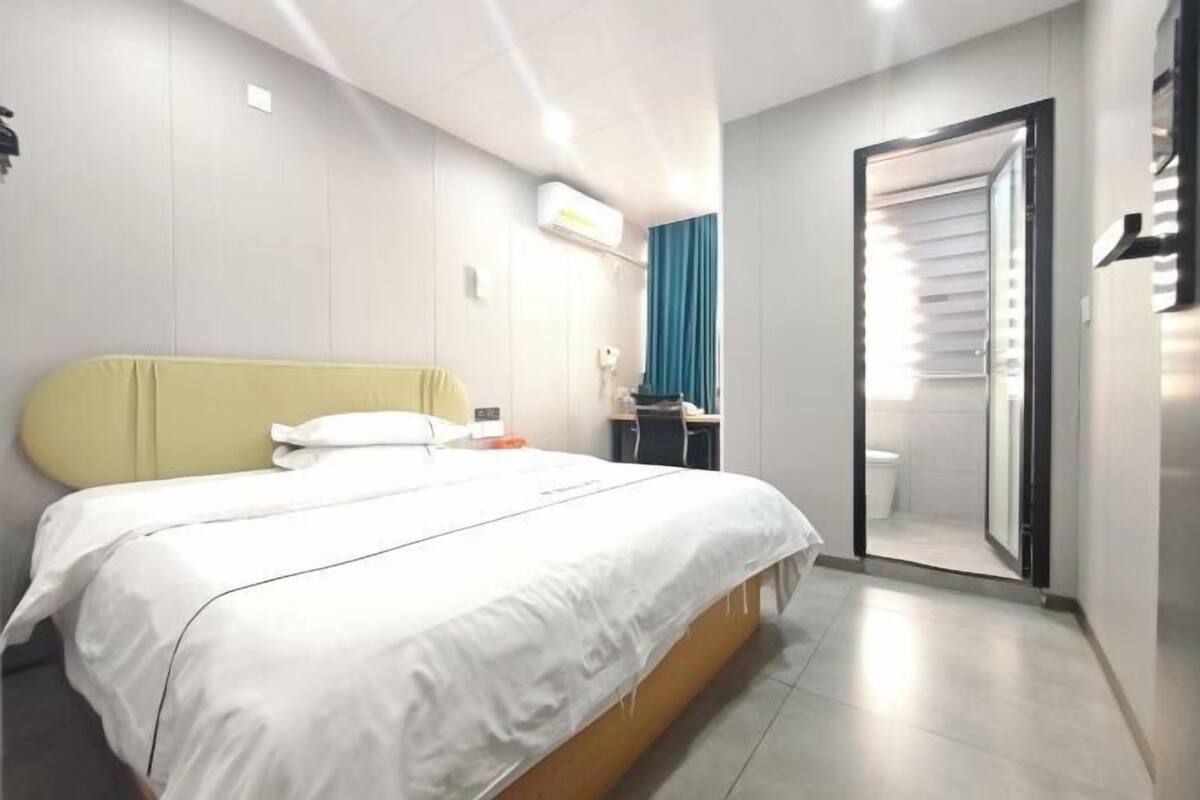 A hotel room with a bed, a desk, a mirror, and a bathroom door.