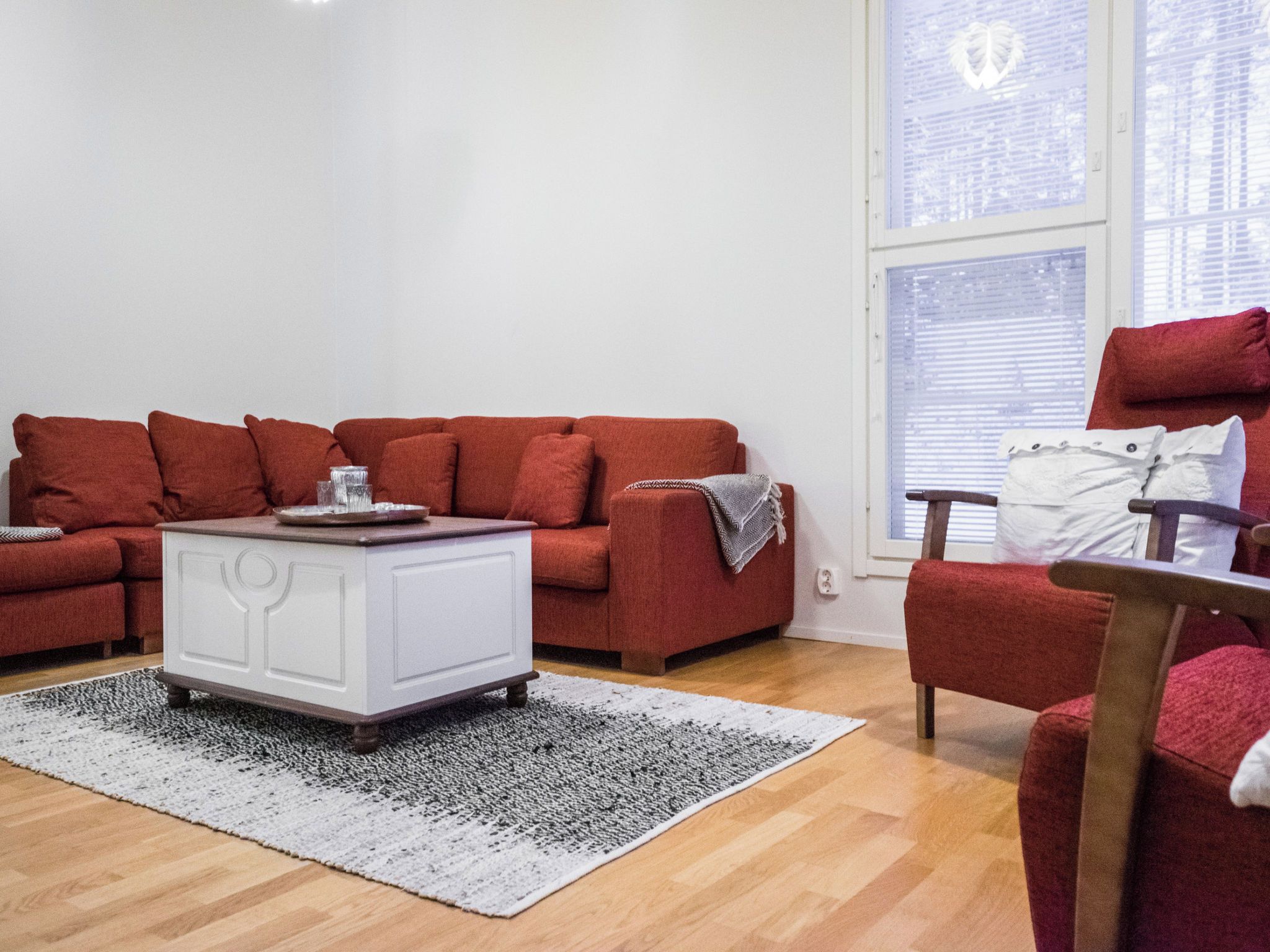 Un salon avec un canapé rouge, un buffet blanc et un tapis à motifs.