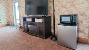 Un soggiorno con una TV a schermo piatto su un mobile, un piccolo frigorifero e un'alta lampada da terra.