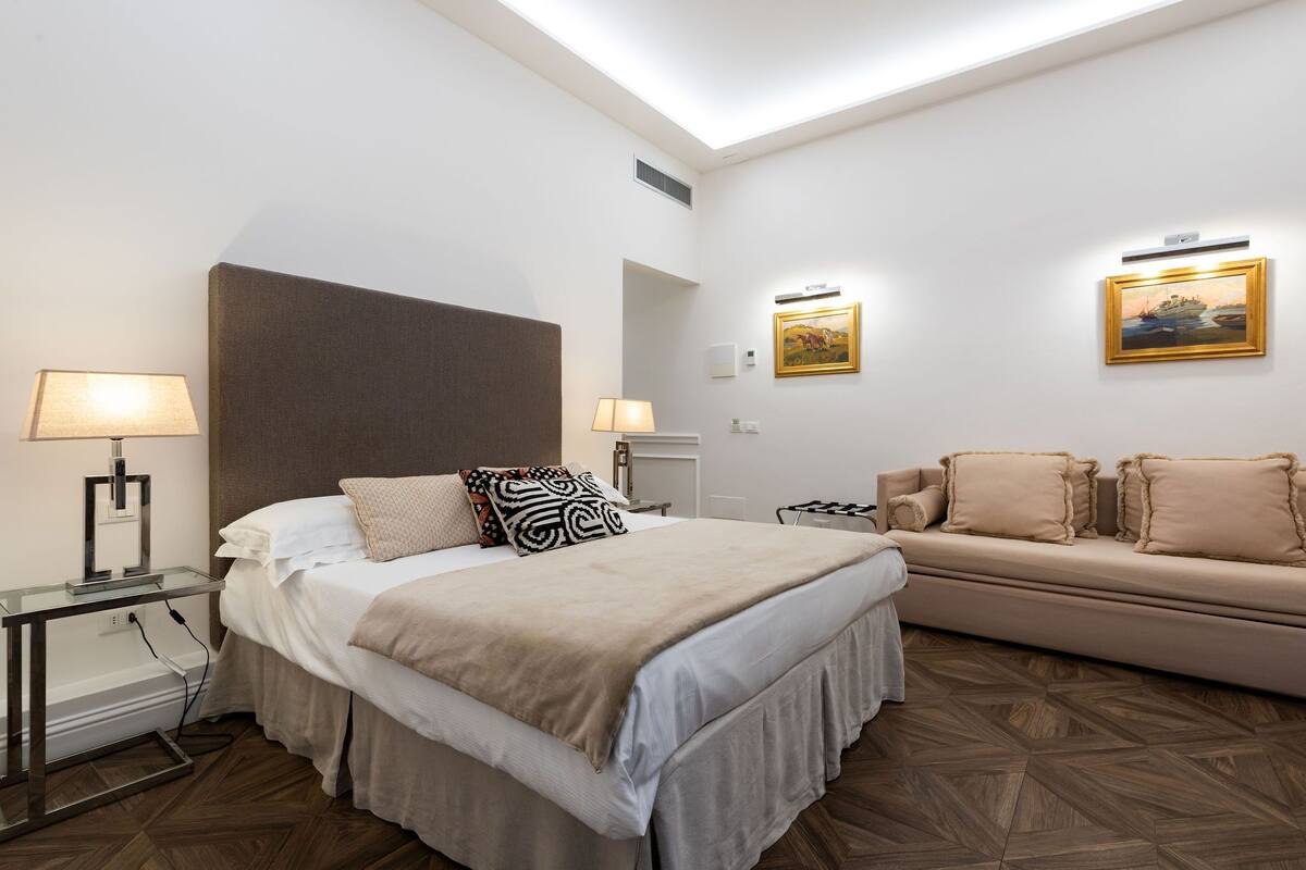 A hotel room with a bed, bedside tables, a sofa, and artwork on the walls.